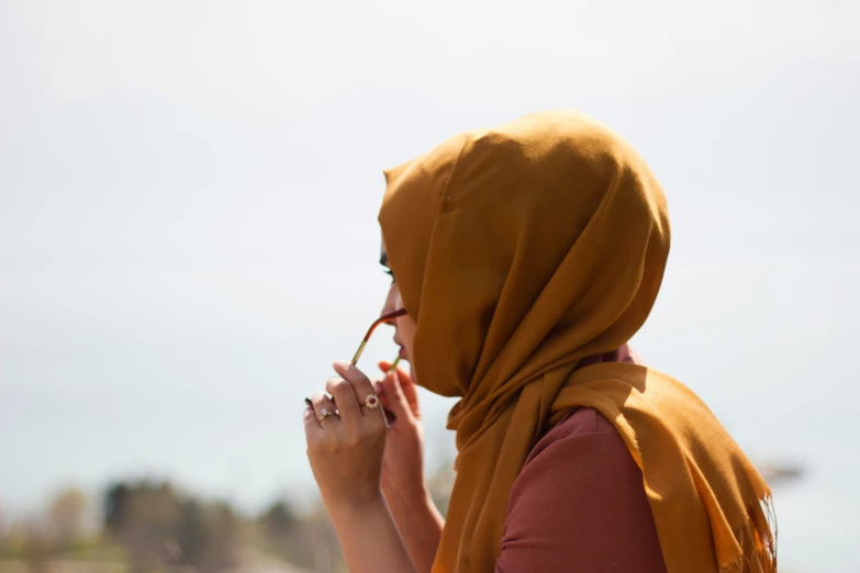 a woman wearing a hijab standing with her hand in her mouth