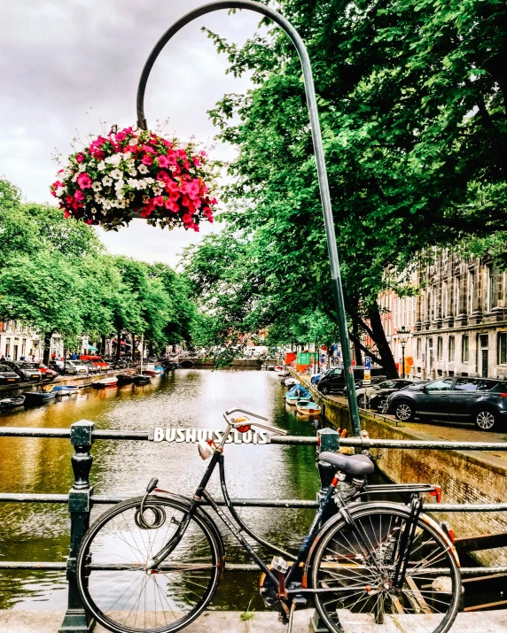 bicycle leaning up against railing with hanging basket over canal