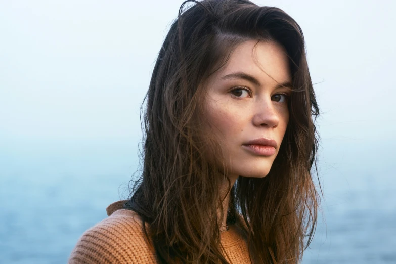 woman with brown sweater standing by the water