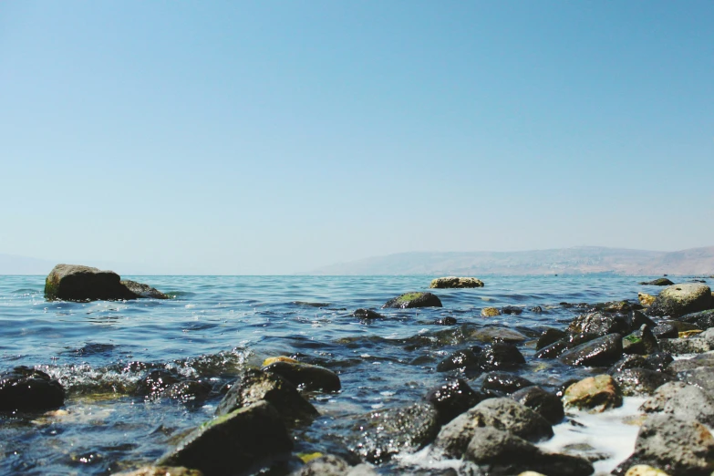 a rocky beach and water with a rock outcropping in the distance