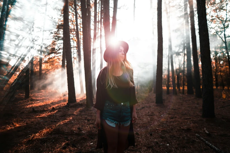 a woman standing in a forest with the sun shining through the trees