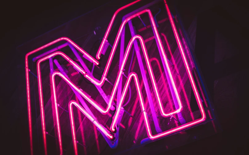 a neon sign in a black room with the letter m on it