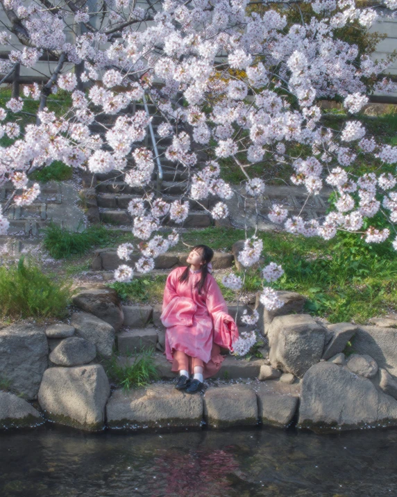 a young woman sitting on a rock wall in front of blossomed trees