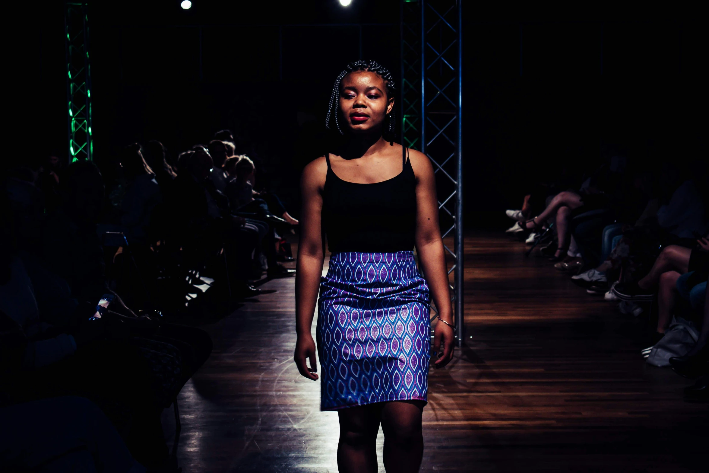 a woman walking down a dark runway with a black top