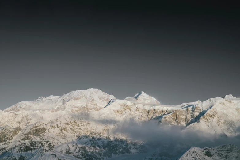 the mountains are covered in snow in front of a dark sky