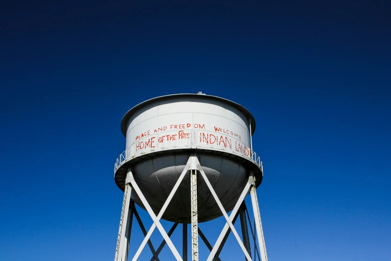 a tall white water tower with graffiti on the side of it