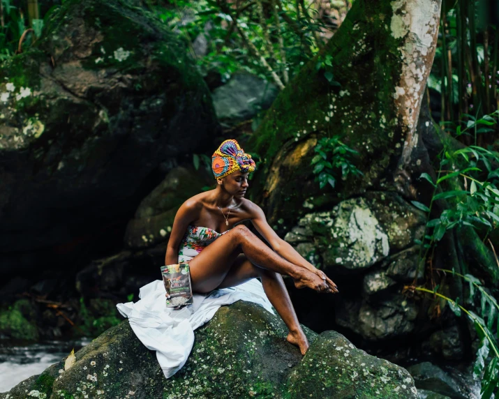 a woman sitting on top of a green rock next to trees