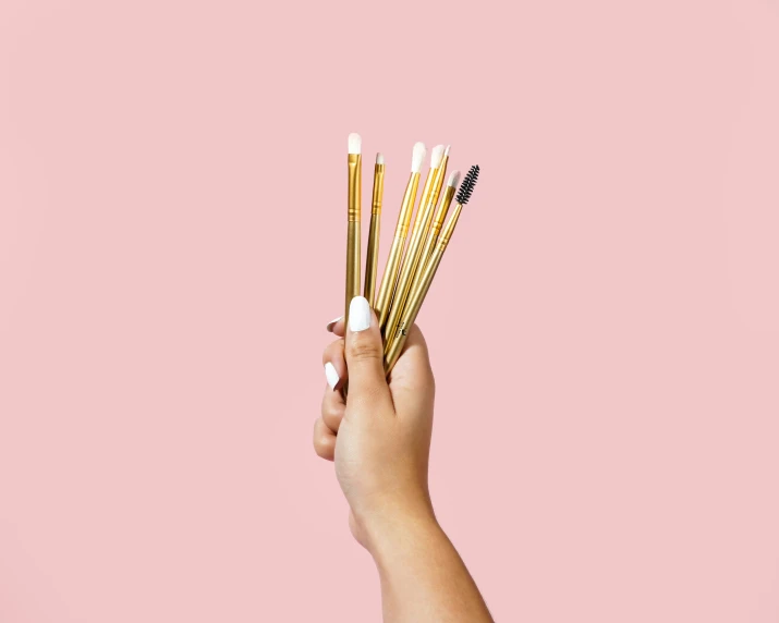 a hand holding several makeup brushes on pink background