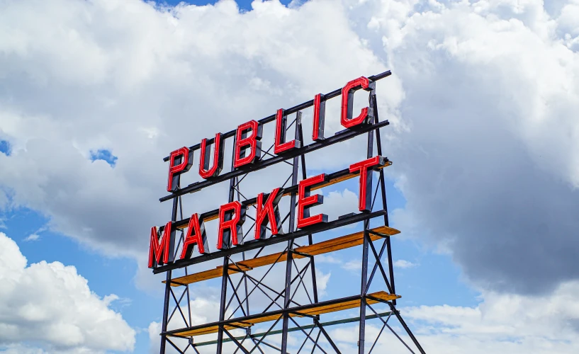 the neon sign says public market in front of a cloudy sky