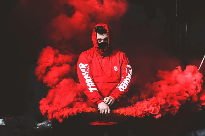 a man wearing red in a black background with red smoke