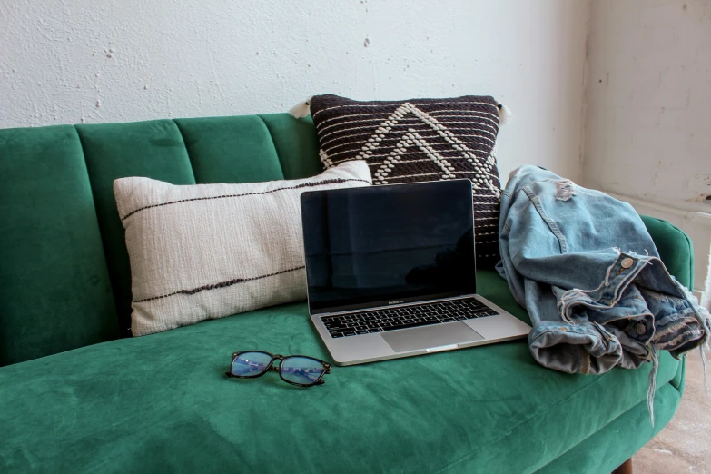 a green couch with a laptop, blanket and sunglasses