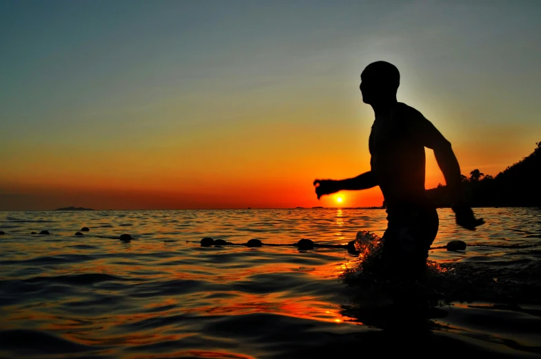 a person walking into the ocean during a sunset