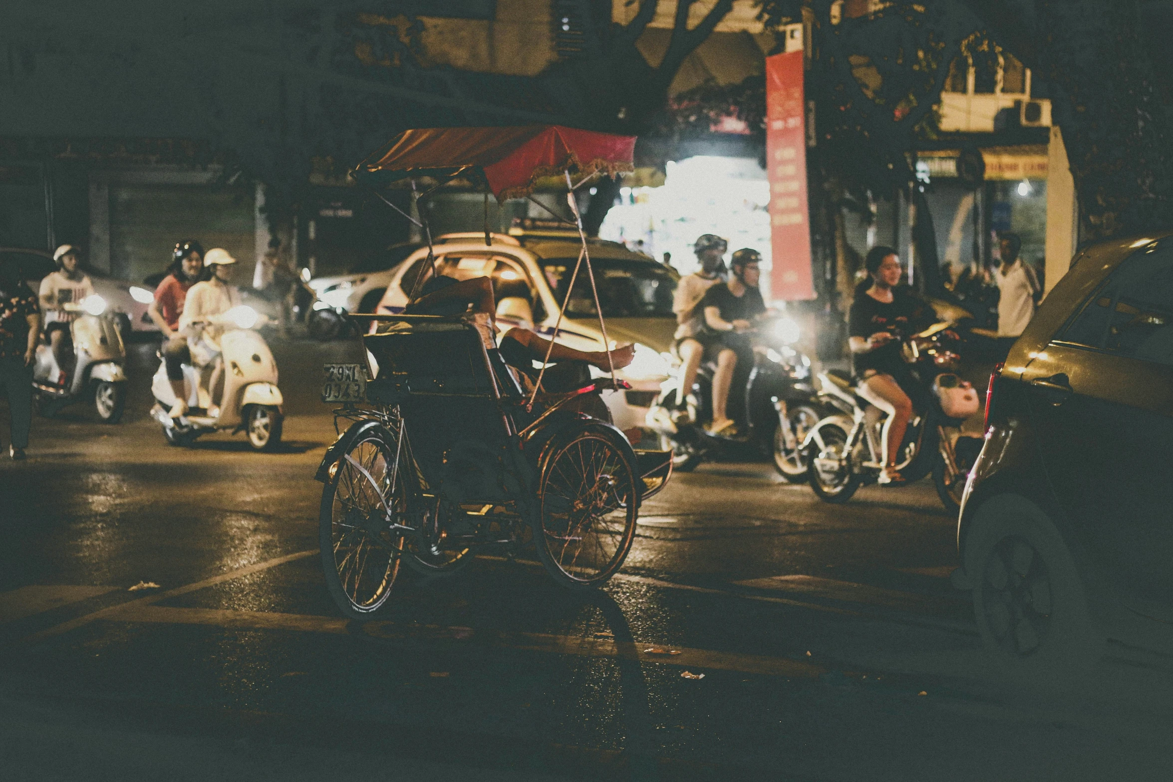 several motor scooters, bicycles, and people on motorcycles at night