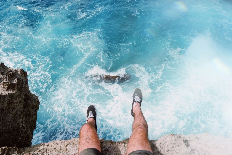 the legs and feet of a person on top of a cliff by the ocean