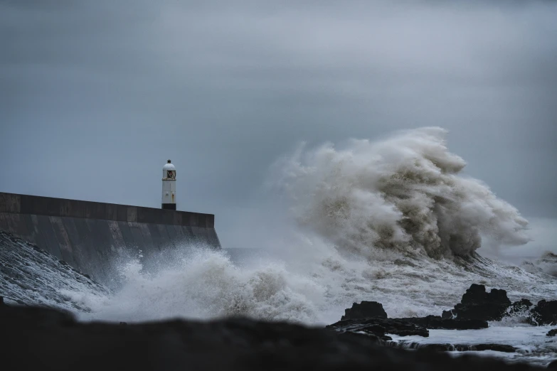 huge waves crashing against the stone wall with lighthouse