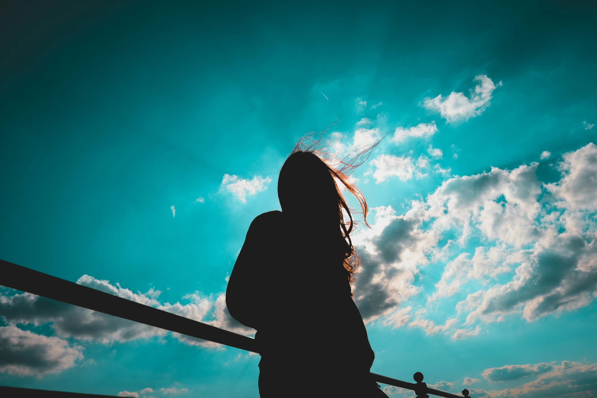 there is a female silhouette holding a skate board under a blue sky with fluffy clouds