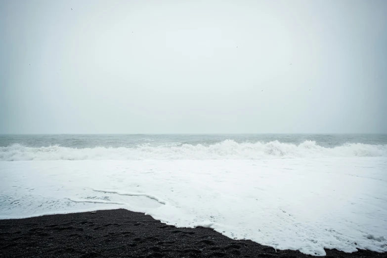 an ocean with the waves crashing on the black sand