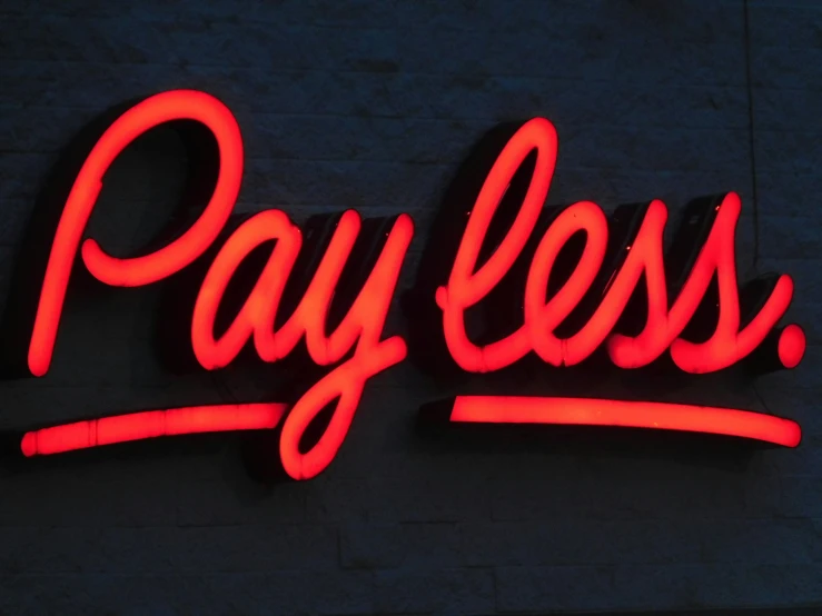 a neon sign reading pay less on the side of a building