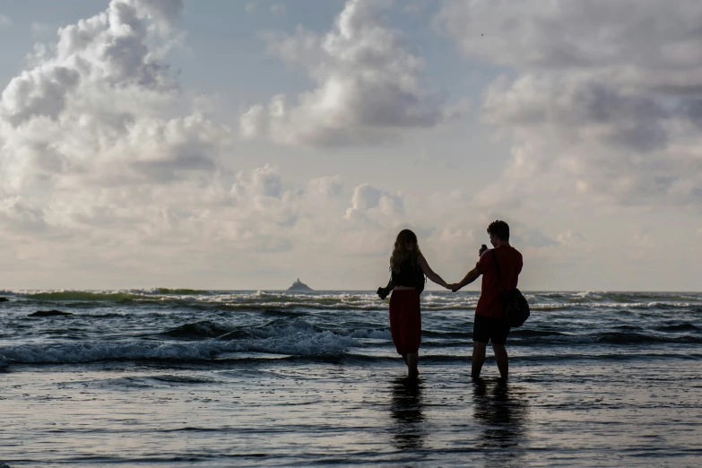 two women walking through the ocean on a beach holding hands