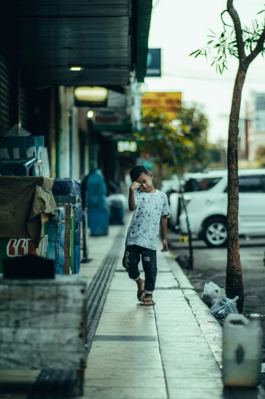 a little boy standing on a sidewalk talking on a cell phone