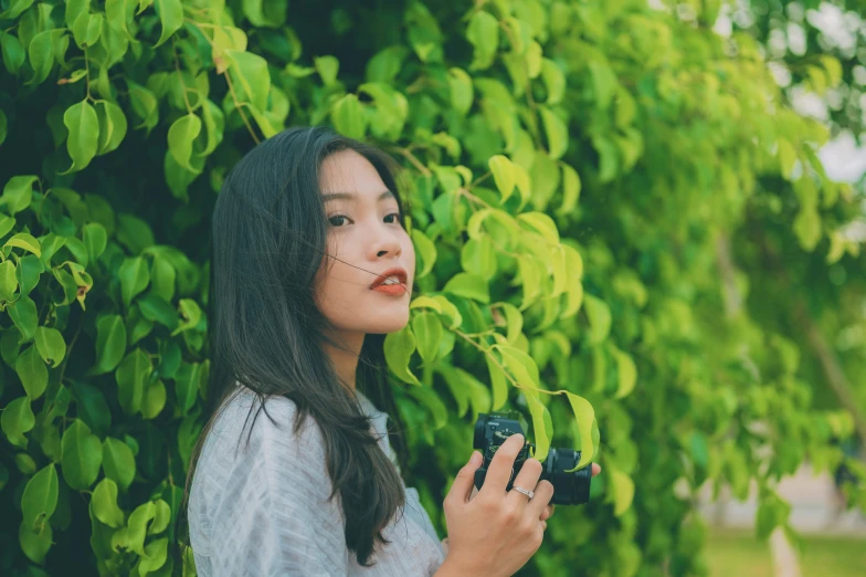 an asian woman standing under a tree holding a cell phone