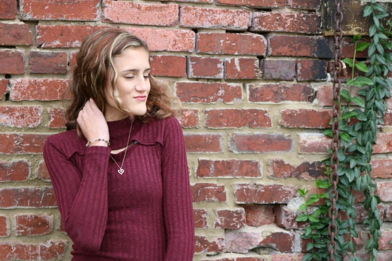 a woman in a burgundy sweater poses next to a brick wall