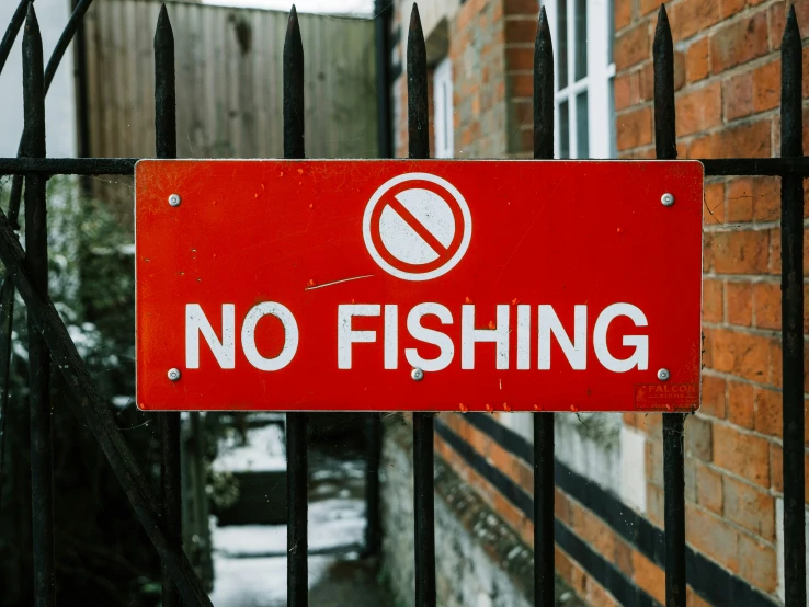 a red sign that says no fishing is hanging from the iron fence