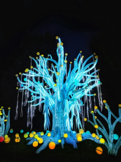 colorful illuminated trees stand in the dark, with various colored balls all around them
