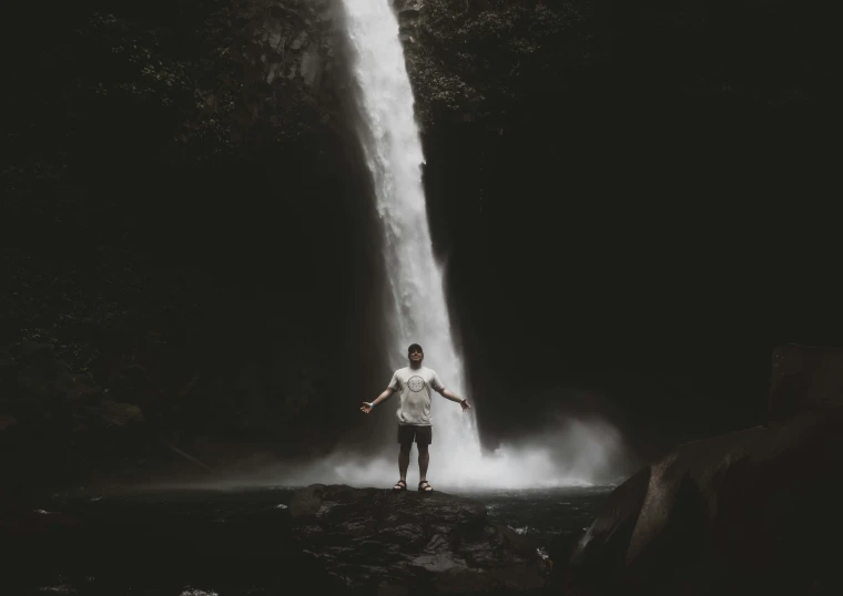 man in white shirt standing near waterfall in large open area