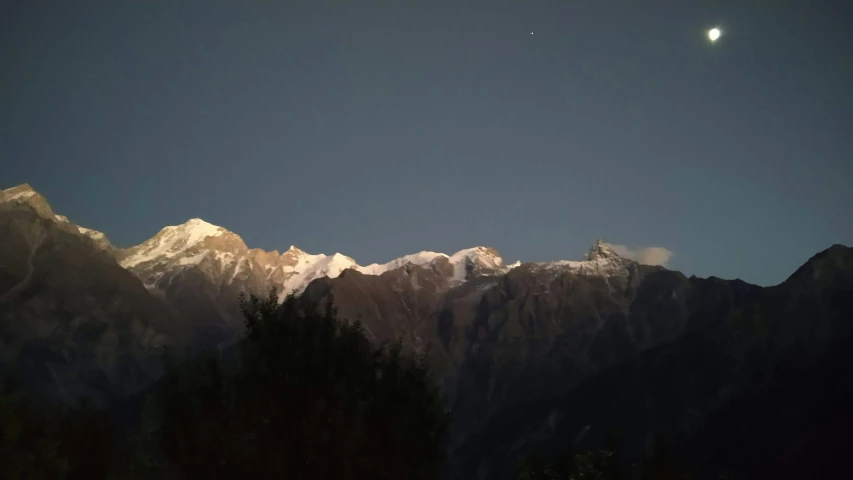 the moon shines in front of a dark mountain