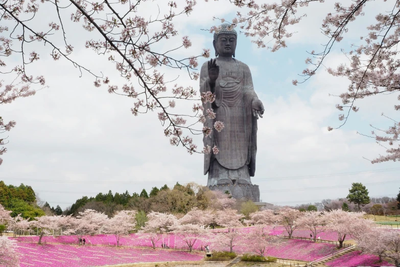 large stone statue sitting next to trees covered with pink flowers