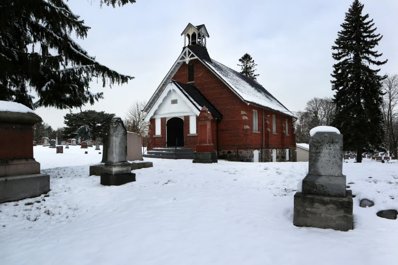 a church with graves in the snow next to evergreen trees