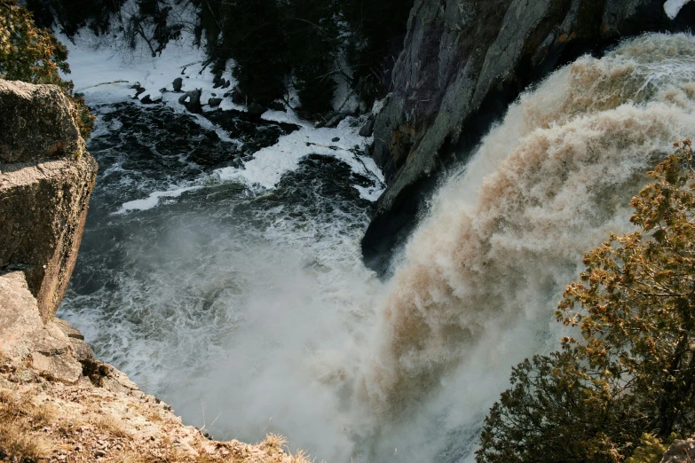 a large waterfall and brown water is surrounded by snow