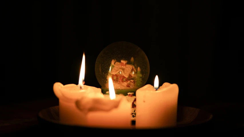 three candles sit in front of an empty glass globe