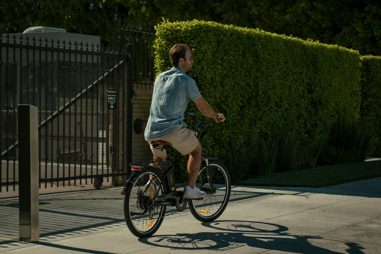 man on bicycle next to sidewalk with fencing and gate