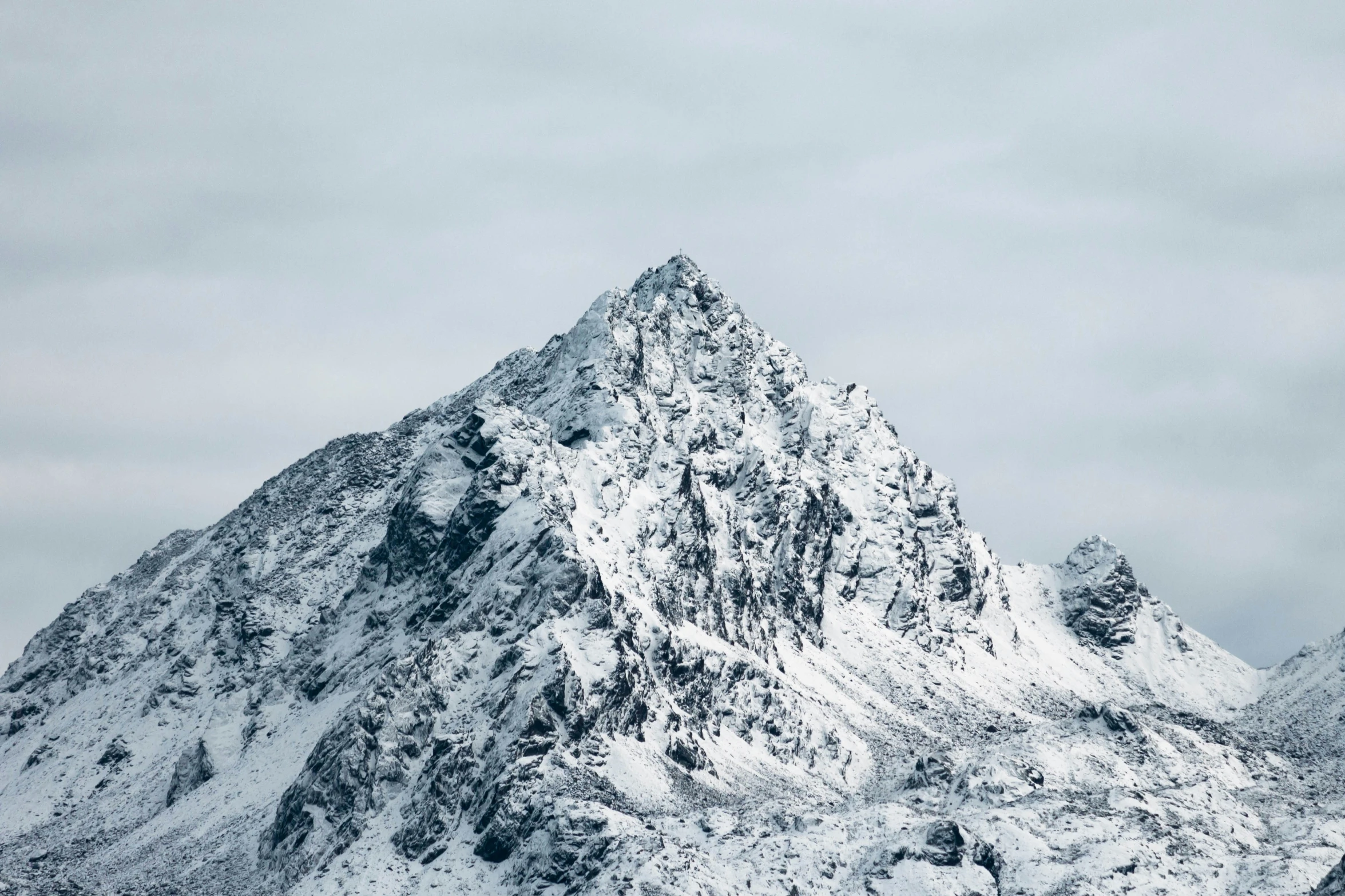 a snow covered mountain peak under grey skies