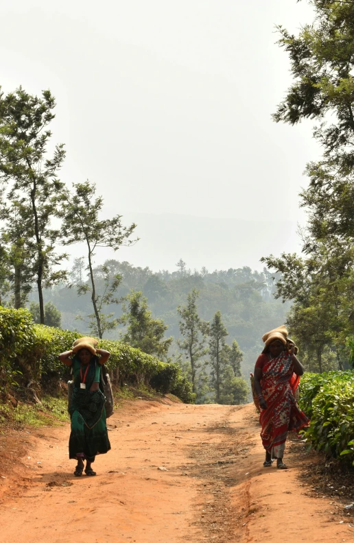 two women in colorful dresses carrying baskets down a dirt path