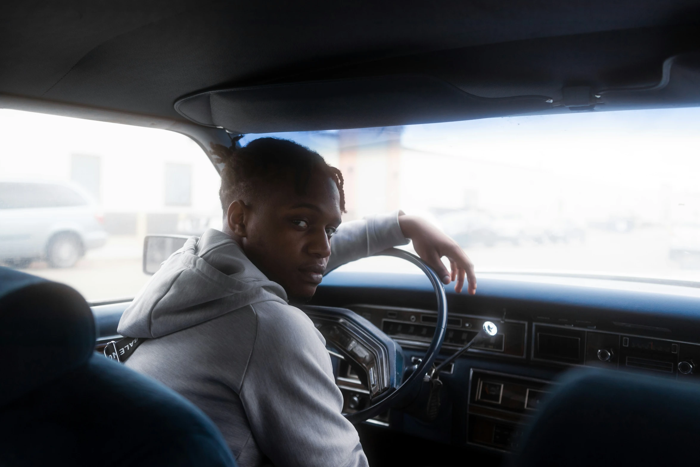 a man in a car with a hoodie and a car steering wheel