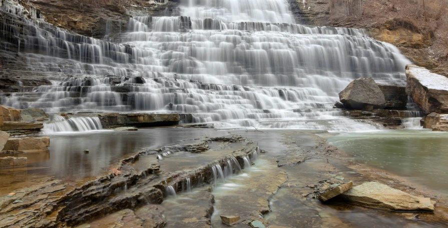 a small waterfall with rocks in the foreground and water pouring over the falls