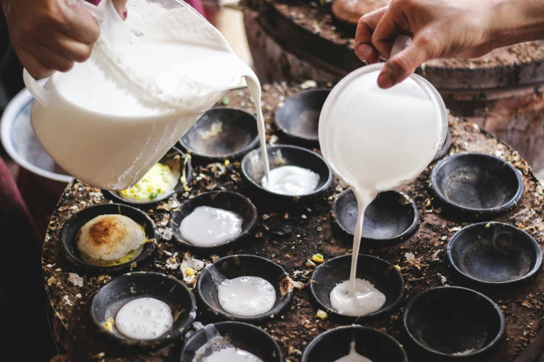 a person pouring milk into a bowl next to a bunch of cups