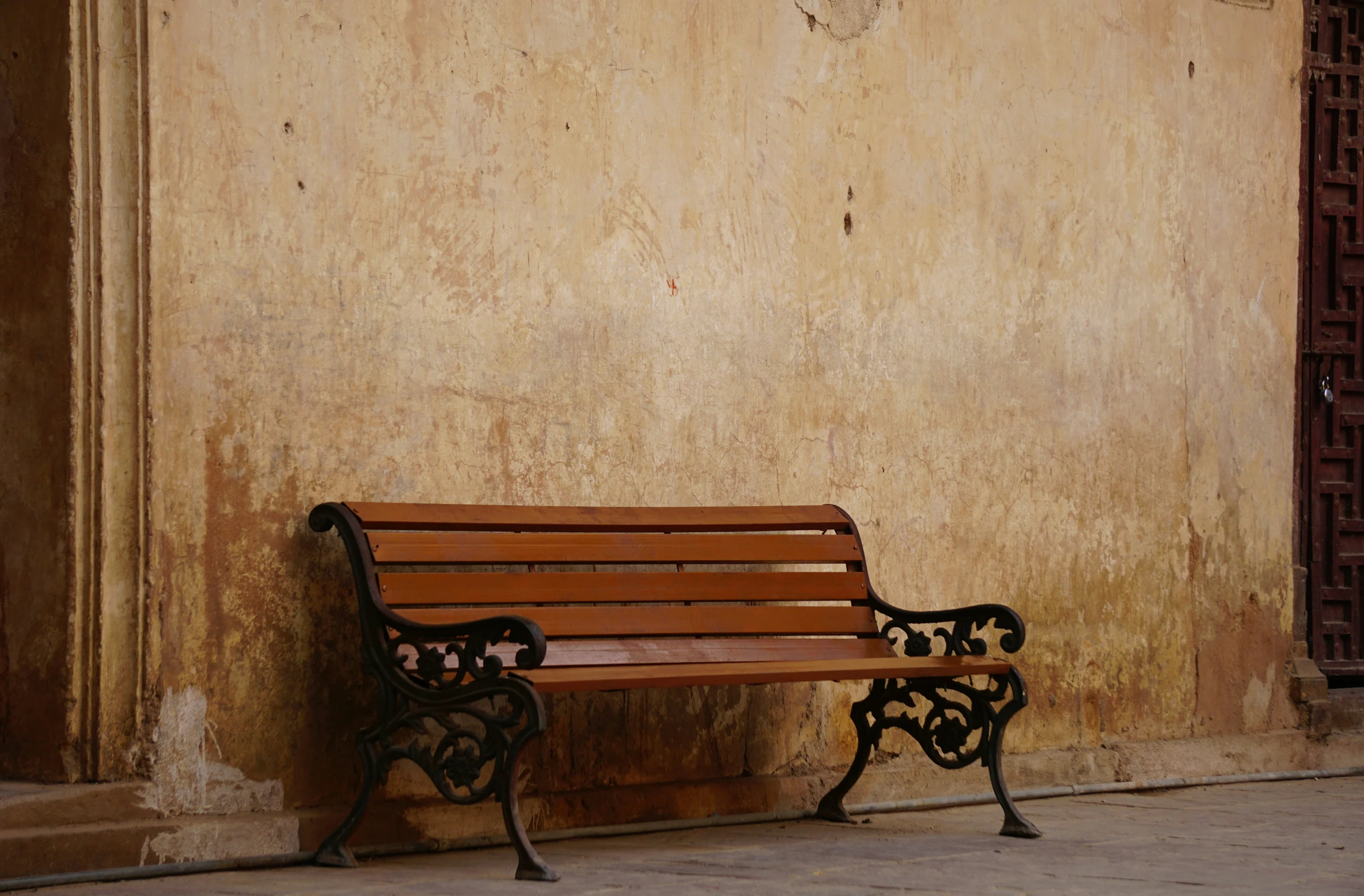 a bench on a street side with a brown wall in the background