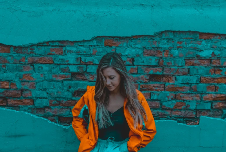 a woman with long hair standing near a brick wall