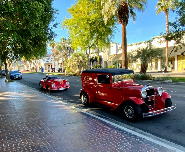 two classic red cars driving down a street