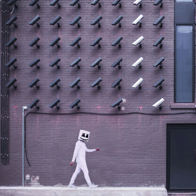 a man walks past surveillance cameras on the side of a building