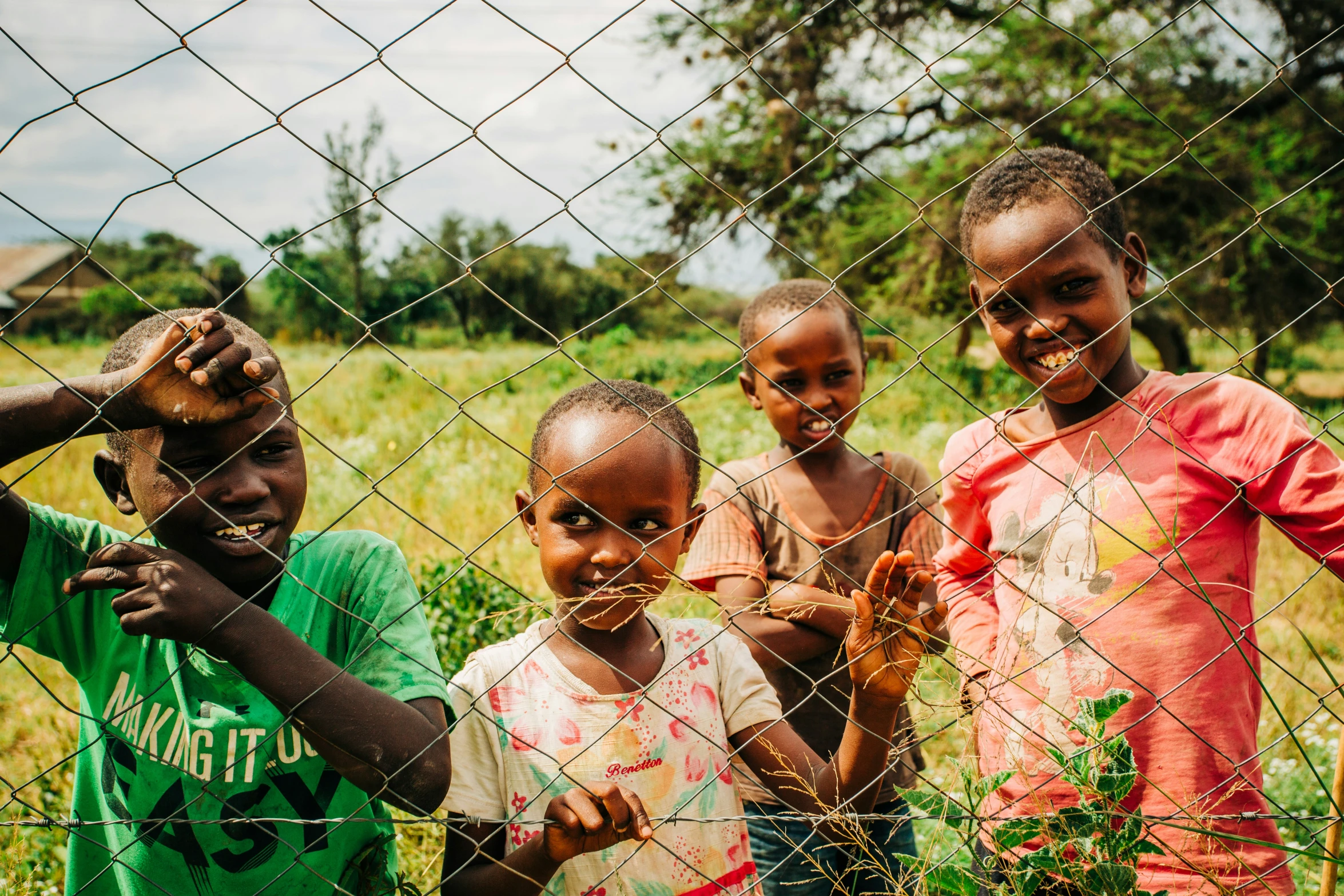 four young children standing behind a fence and smiling