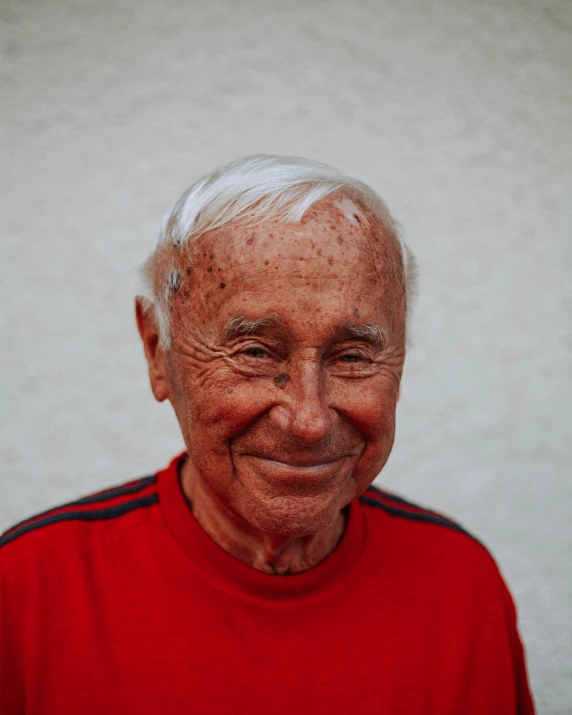 an old man smiling and wearing a red shirt