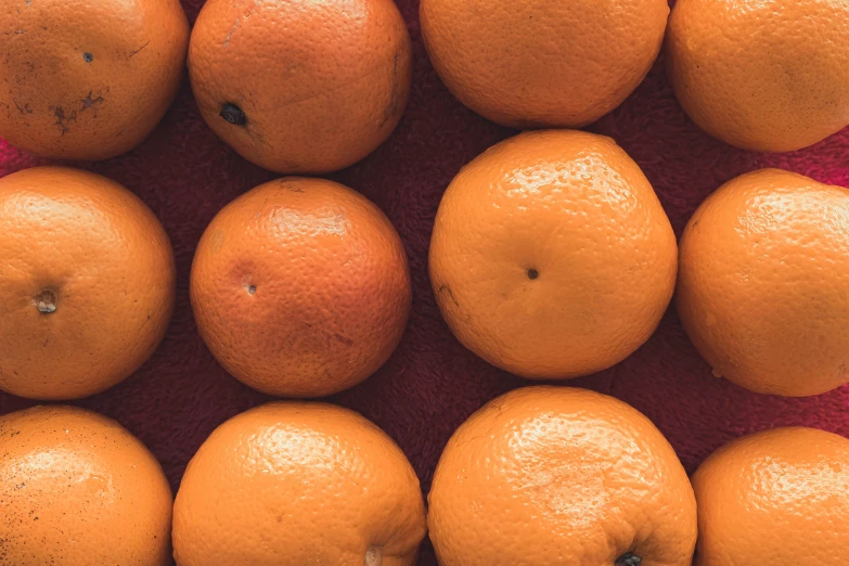 there are many oranges in an arrangement on top of a red cloth