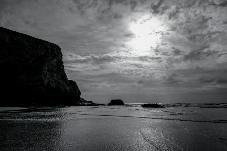 an empty beach with the sun shining on a large rock