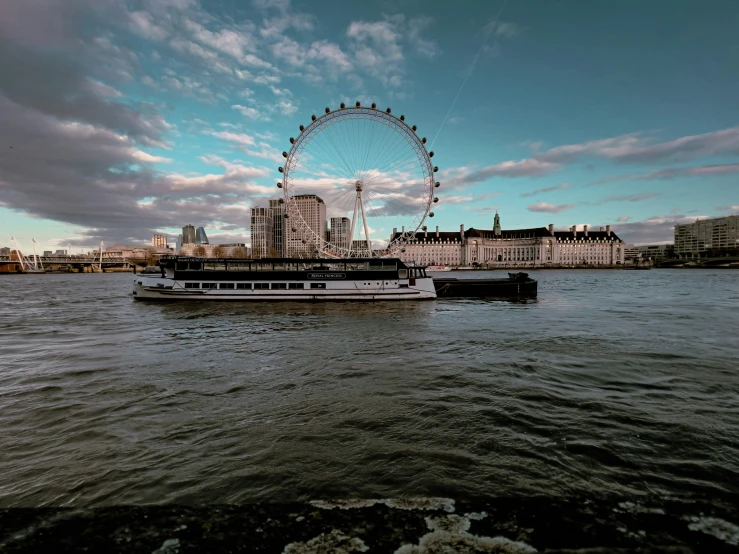 a boat floating down a river with a large ferris wheel behind it