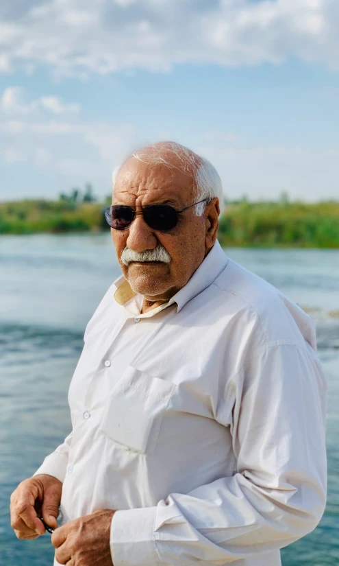 a man standing by the water in a white shirt and sunglasses